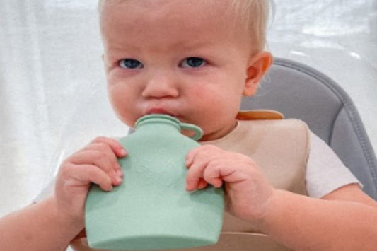 Baby holding and drinking from a green Palmetto Pouch while sitting in a high chair.