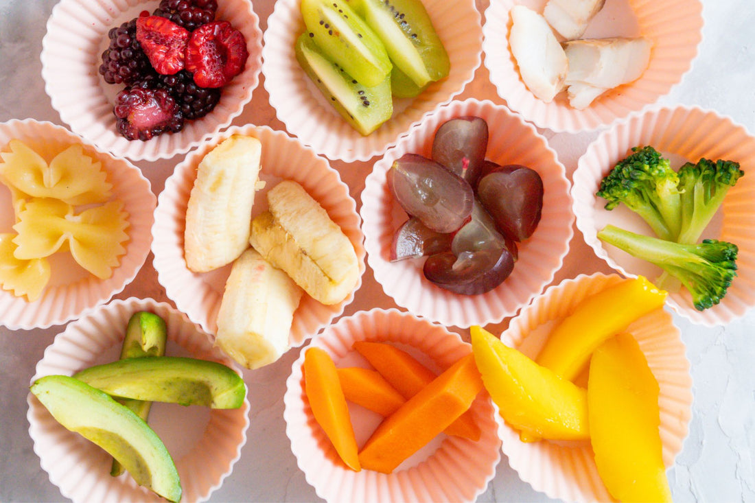 An assortment of colorful fruits and vegetables arranged in silicone cups, including avocado, kiwi, broccoli, and bananaâperfect for introducing solids.