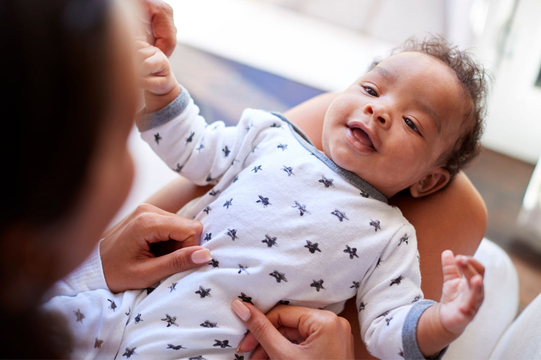 A happy baby in a white onesie with star patterns, being gently held by a parent, highlighting the importance of eco-friendly baby products for babies.