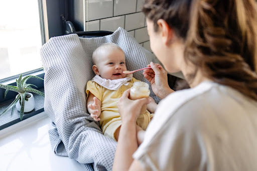 A mother feeds her baby a jar of baby food