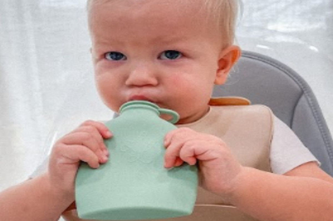 Baby holding and drinking from a green Palmetto Pouch while sitting in a high chair.