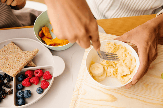 A busy mom preparing easy baby food recipes with mashed bananas and fresh berries.