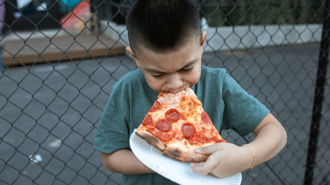 Young child eating a slice of pepperoni pizza, representing processed food choices.