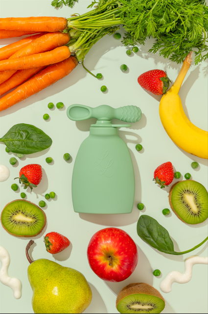 Colorful assortment of fresh fruits and vegetables, including carrots, bananas, apples, and kiwi, with a reusable food pouch in the center.