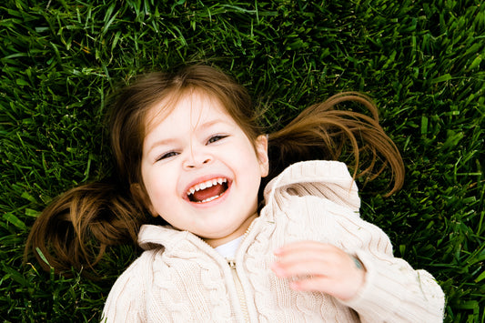 A happy child laying on the grass, smiling brightly, highlighting the benefits of reusable pouches, such as convenience and promoting a healthy, active lifestyle.