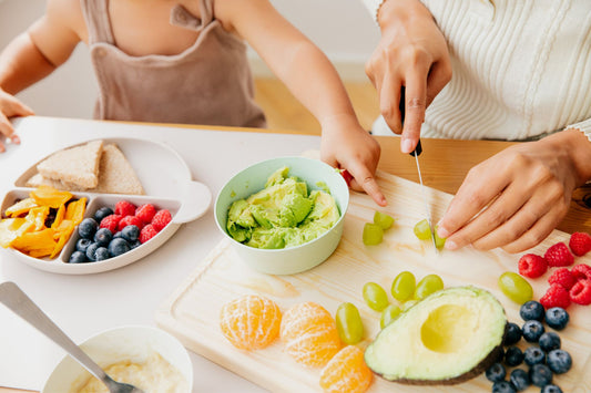 A parent follows the baby food stages, preparing a variety of fresh foods including avocado, grapes, and berries for their toddler.