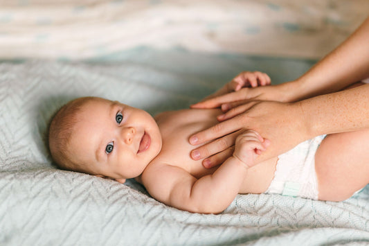 Smiling 8-month-old baby receiving a gentle tummy massage from a parent's hands, highlighting a moment of bonding and comfort.