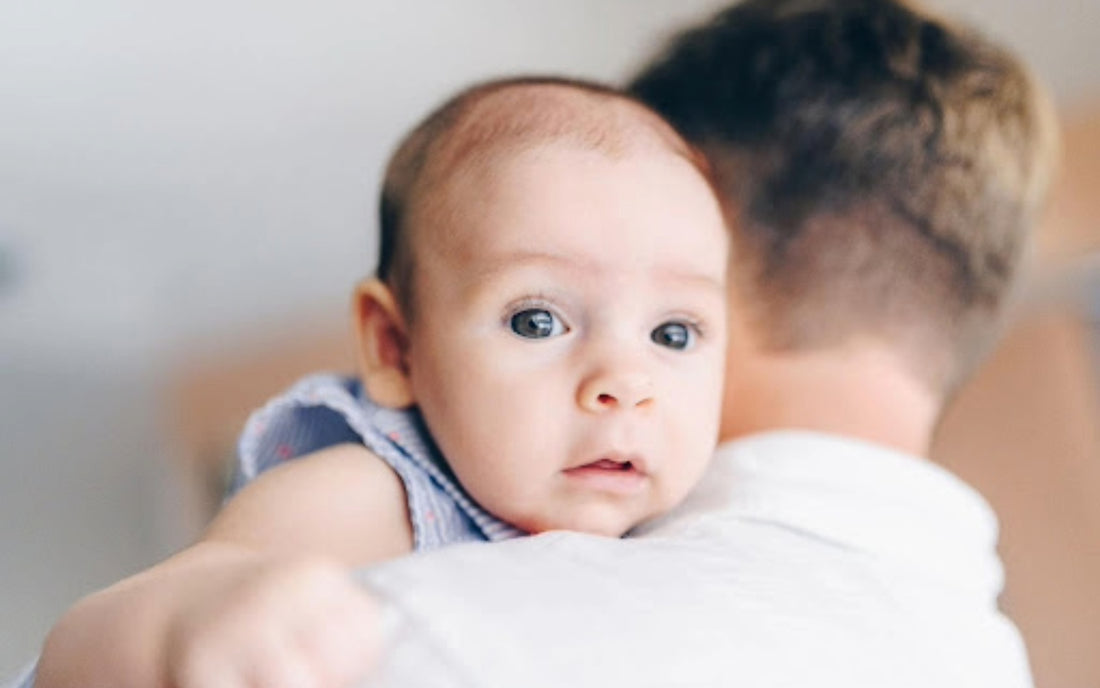 A 4-month-old baby with alert eyes being held over a caregiver's shoulder, anticipating feeding time.