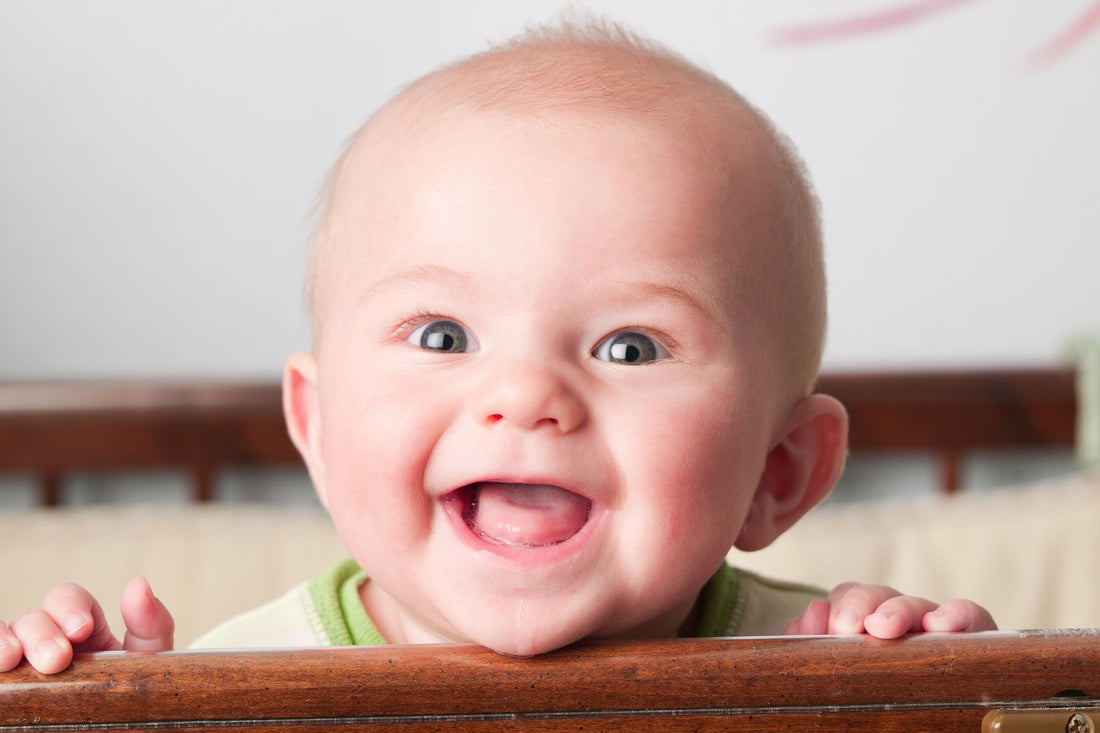 A smiling baby holding onto the edge of a crib, showcasing the importance of non-toxic baby products for mental health.