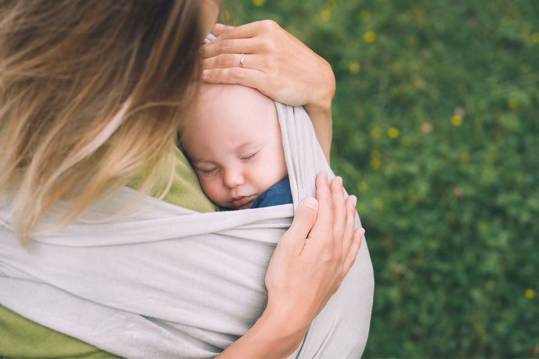 A mom holds her baby in an organic carrier, an example of sustainable baby gear.