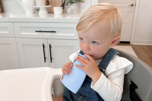 Toddler girl drinking from a blue Palmetto Pouch in a high chair, emphasizing the impact of a healthy childhood diet on long-term health.