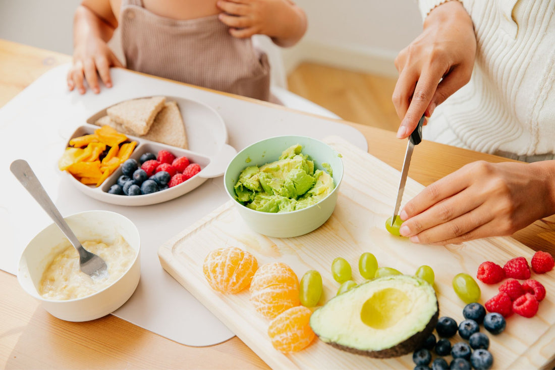 A mom cuts up baby-led weaning foods while her toddler looks on.